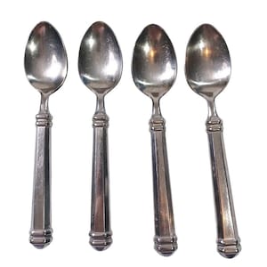 May include: Four silver spoons with oval bowls and faceted handles. The spoons have a classic design, with a decorative band near the bowl and at the end of the handle. The spoons are arranged on a white background.