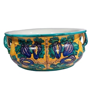 May include: A large, yellow ceramic bowl with green and blue painted fig designs. The bowl has two handles and a white interior.