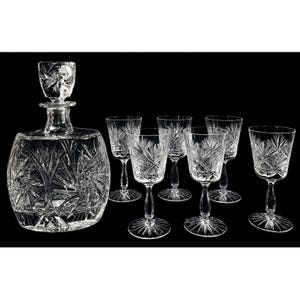 May include: A clear glass decanter with a matching stopper and five matching stemmed glasses. Each piece features a deep, intricate starburst and fan cut pattern across the surface, reflecting light with a brilliant, multifaceted appearance.