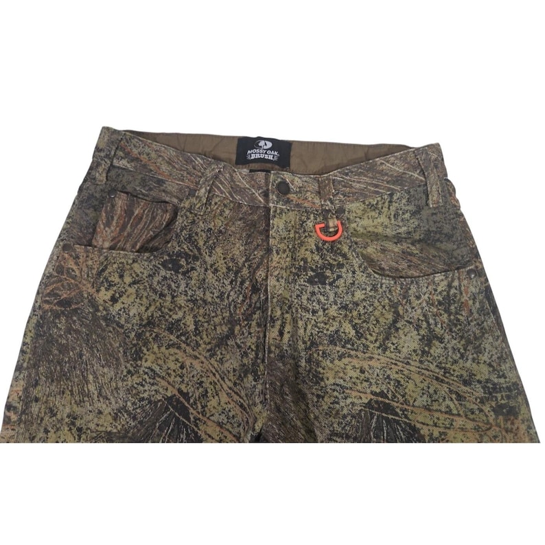 May include: Camouflage pants with a button closure, front pockets, and an orange loop. The pants feature a brown, green, and tan pattern. The Mossy Oak brand name is visible on the waistband.