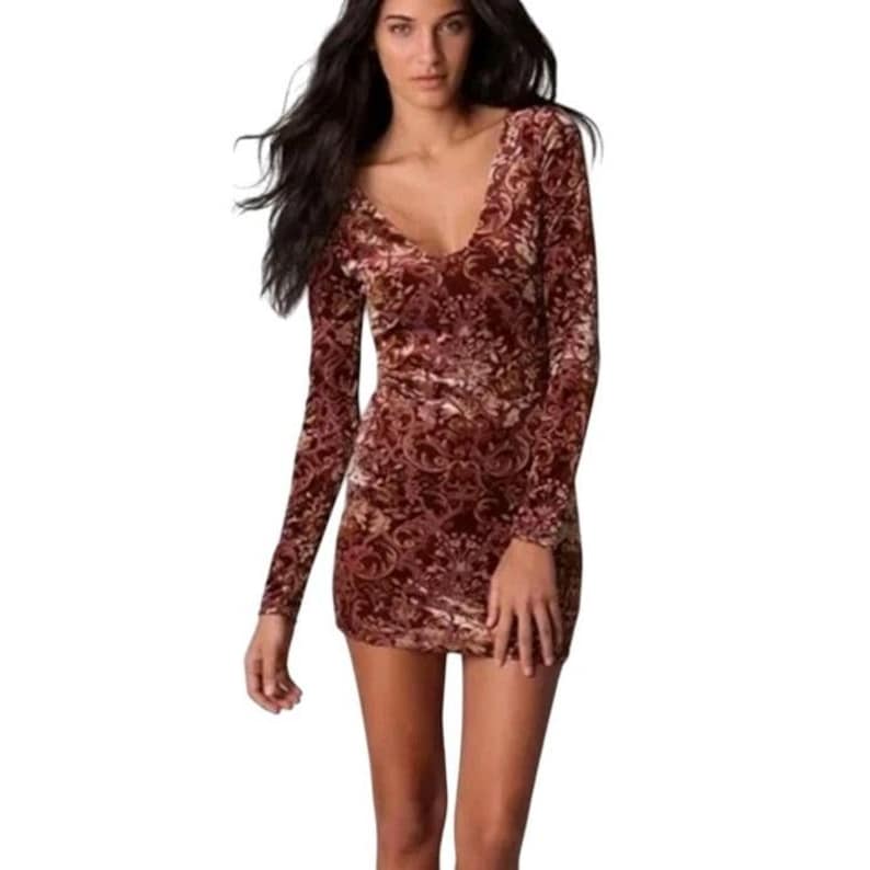 May include: A burgundy velvet mini dress with long sleeves and a deep V-neck. The dress features a subtle floral pattern in shades of gold and brown. The dress is form-fitting and reaches mid-thigh.