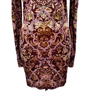 May include: A long-sleeved dress with a burgundy and brown floral pattern. The dress features a detailed design with light purple and tan accents. The fabric appears to be soft and has a velvet-like texture.
