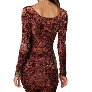 May include: A long-sleeved, bodycon dress with a burgundy and gold floral pattern. The dress features a scoop neckline and fitted silhouette. The fabric has a velvet-like texture, and the sleeves are long, ending at the wrists.
