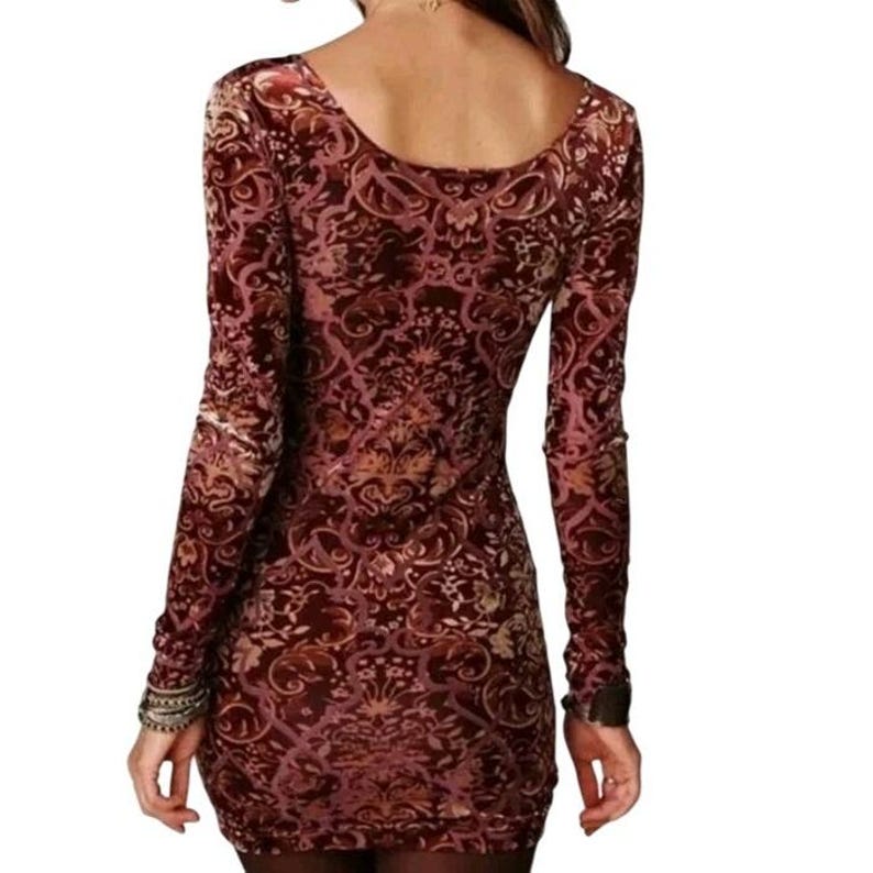 May include: A long-sleeved, bodycon dress with a burgundy and gold floral pattern. The dress features a scoop neckline and fitted silhouette. The fabric has a velvet-like texture, and the sleeves are long, ending at the wrists.