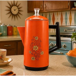 May include: A tall, cylindrical orange percolator coffee pot featuring a black handle and a clear glass knob on the lid. The body is decorated with a black and yellow floral pattern consisting of swirling vines and small daisy-like flowers.