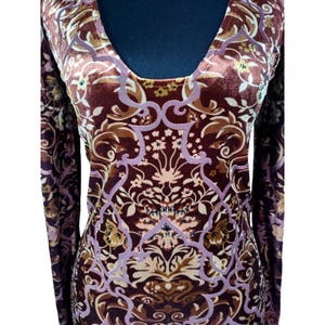 May include: A long-sleeved, scoop-neck top with a velvet texture. The top features a repeating floral pattern in shades of brown, tan, and lavender. The design is symmetrical and covers the entire garment, creating a vintage aesthetic.