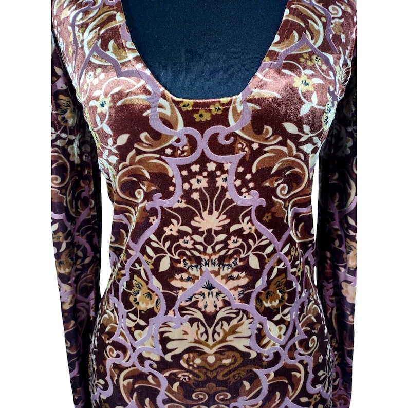 May include: A long-sleeved, scoop-neck top with a velvet texture. The top features a repeating floral pattern in shades of brown, tan, and lavender. The design is symmetrical and covers the entire garment, creating a vintage aesthetic.