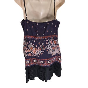 Puede incluir: Un top camisero azul marino con estampados florales y cachemir en tonos naranja, blanco y marr&oacute;n. El top presenta finas correas negras y un dobladillo de encaje negro. La tela parece ligera.