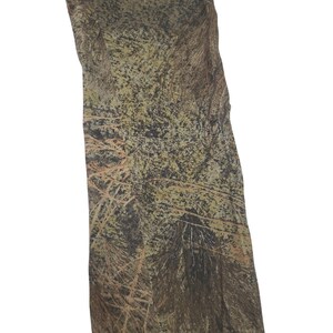 May include: Camouflage fabric with a mix of green, brown, and tan colors. The pattern resembles a forest with branches and leaves. The fabric is likely used for hunting or outdoor apparel.