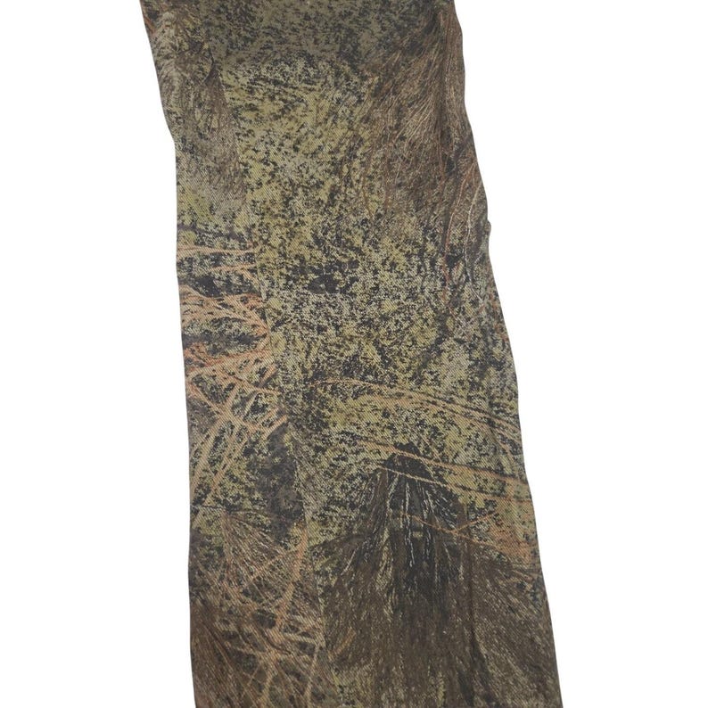 May include: Camouflage fabric with a mix of green, brown, and tan colors. The pattern resembles a forest with branches and leaves. The fabric is likely used for hunting or outdoor apparel.