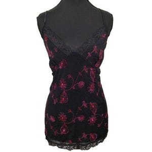 May include: Black camisole with a V-neck and spaghetti straps. The top is adorned with pink floral embroidery and lace trim along the neckline and hem. The camisole is displayed on a black mannequin.