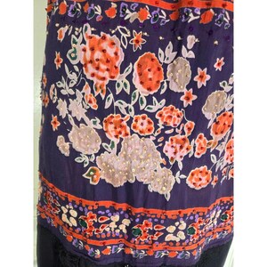 Puede incluir: Prenda morada oscura con un intrincado estampado floral en naranja, blanco y rosa. El dise&ntilde;o incluye detalles de cuentas y un borde decorativo. El borde inferior presenta un ribete de encaje negro.