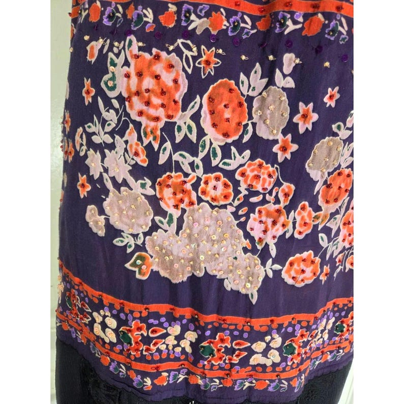 Puede incluir: Prenda morada oscura con un intrincado estampado floral en naranja, blanco y rosa. El dise&ntilde;o incluye detalles de cuentas y un borde decorativo. El borde inferior presenta un ribete de encaje negro.