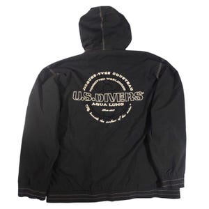 May include: Black hooded jacket with white stitching and a drawstring hem. The back features a white circular graphic with the text "JACQUES-YVES COUSTEAU COMMITTED WORLDWIDE U.S. DIVERS AQUA LUNG" and the phrase "beneath the surface of the water."
