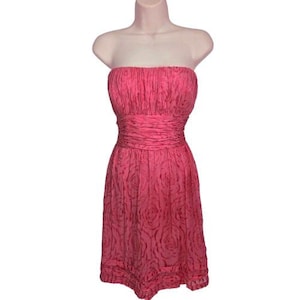 May include: A strapless, knee-length dress in a vibrant pink hue. The bodice features a ruched design, with a cinched waist and a skirt adorned with a subtle rose pattern. The dress is displayed on a mannequin.