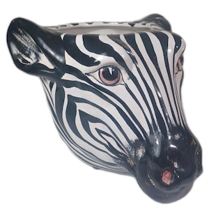 May include: A ceramic planter shaped like a zebra's head. The planter is painted with black and white stripes, with pink accents around the eyes and nose. The zebra head is a unique decorative item.