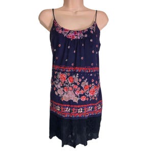 Puede incluir: Vestido lencero azul marino con estampado floral y ribete de encaje. El vestido presenta finos tirantes espagueti, un escote redondo y un estampado floral en tonos rojos, rosas y morados. La parte inferior del vestido tiene un ribete de encaje negro.