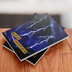 May include: Two black and white notebooks with a blue and white lightning bolt design on the cover. The cover text reads "LAB NOTES".