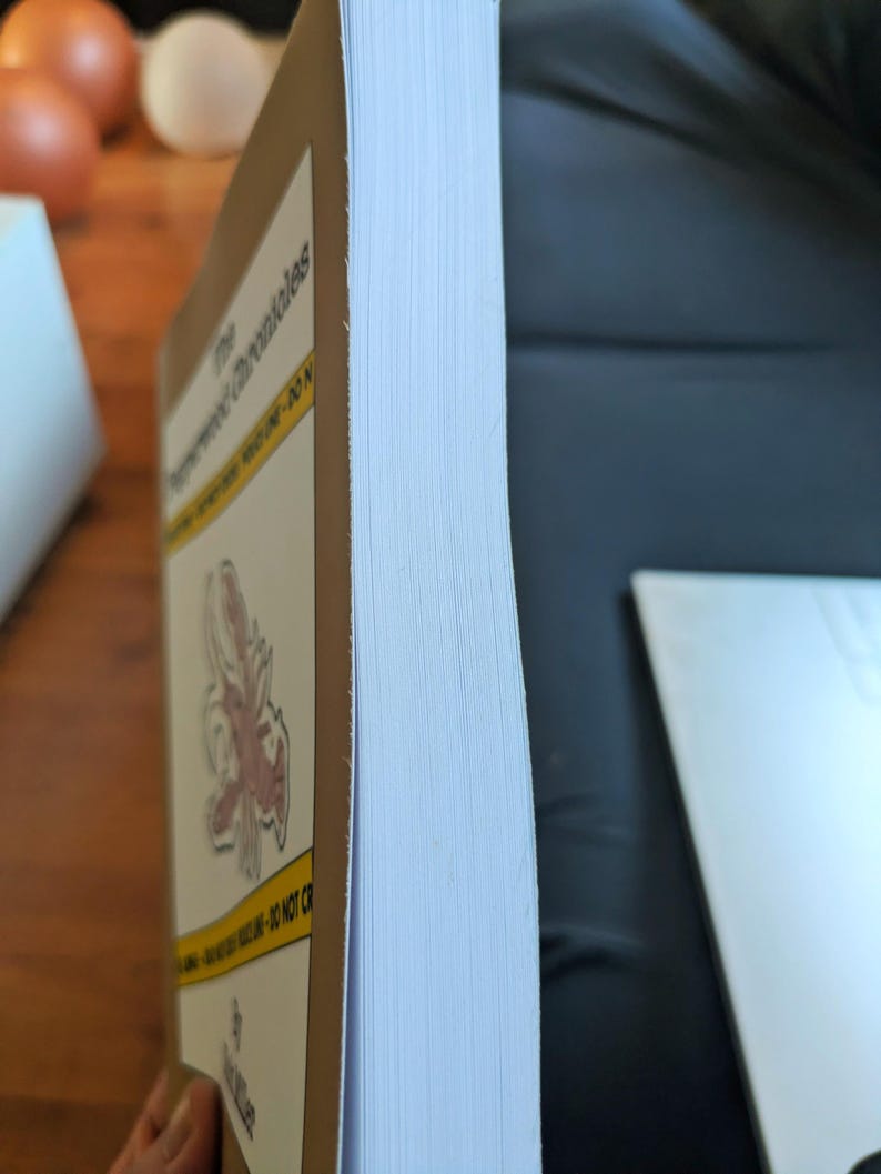 Pu&ograve; includere: Un libro con copertina rigida intitolato "The Brotherhood Chronicles" con una copertina marrone e pagine bianche. Il dorso del libro &egrave; visibile, mostrando lo spessore delle pagine. La copertina presenta una striscia gialla e un'illustrazione rossa e bianca.