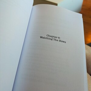 Pu&ograve; includere: Un libro aperto con il testo "Chapter 6: Watching The News" stampato su una pagina bianca. Il libro &egrave; aperto su un capitolo con il numero di pagina 213 visibile. Il libro &egrave; sulle ginocchia di una persona.