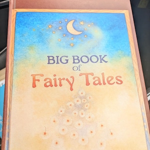 Könnte beinhalten: Ein Hardcover-Buch mit dem Titel "BIG BOOK of Fairy Tales". Das Cover zeigt eine Aquarellillustration eines blauen Himmels mit einem Halbmond und Sternen. Der Titel ist in großen, farbigen Buchstaben mit einem floralen Design gehalten.