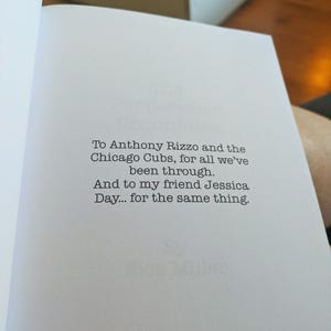 Pu&ograve; includere: Pagina di libro aperta con testo dedicato ad Anthony Rizzo e ai Chicago Cubs, e a Jessica Day. Il testo &egrave; in un semplice font senza grazie, centrato sulla pagina.