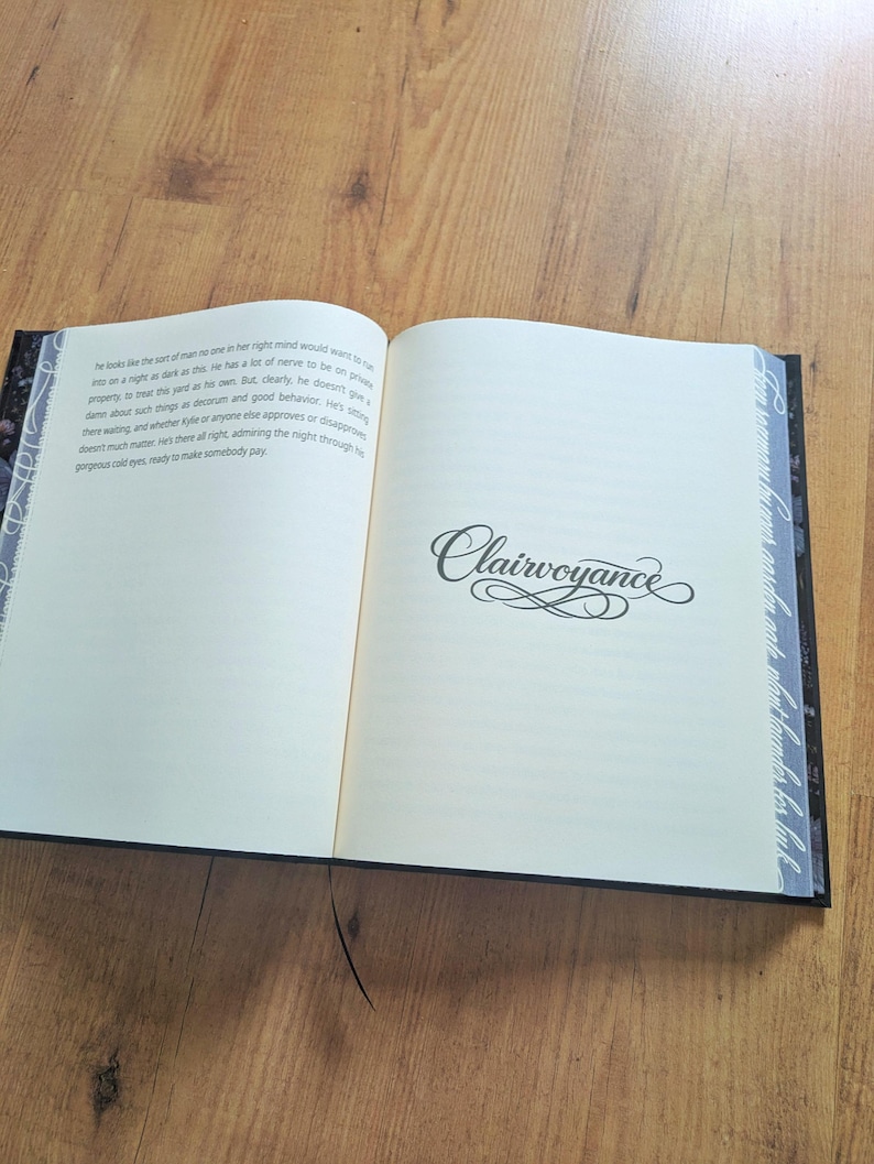 May include: An open book with the word "Clairvoyance" in elegant script on the right page. The left page contains printed text. The book has a black cover with decorative edges and a black bookmark.