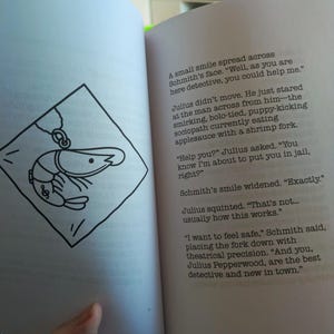 Pu&ograve; includere: Libro aperto con testo e un'illustrazione in bianco e nero di un gambero all'interno di un rombo. Il testo descrive una storia di detective con dialoghi.