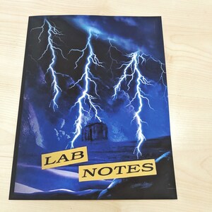 May include: A black notebook with a blue and black lightning storm design. The words "LAB NOTES" are printed in yellow on the cover.