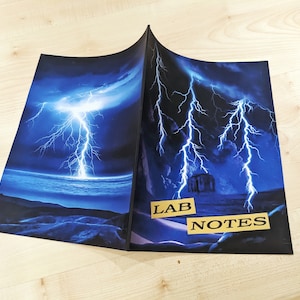 May include: A black notebook with a blue lightning bolt design on the cover. The cover has the words "LAB NOTES" printed on it in gold letters.