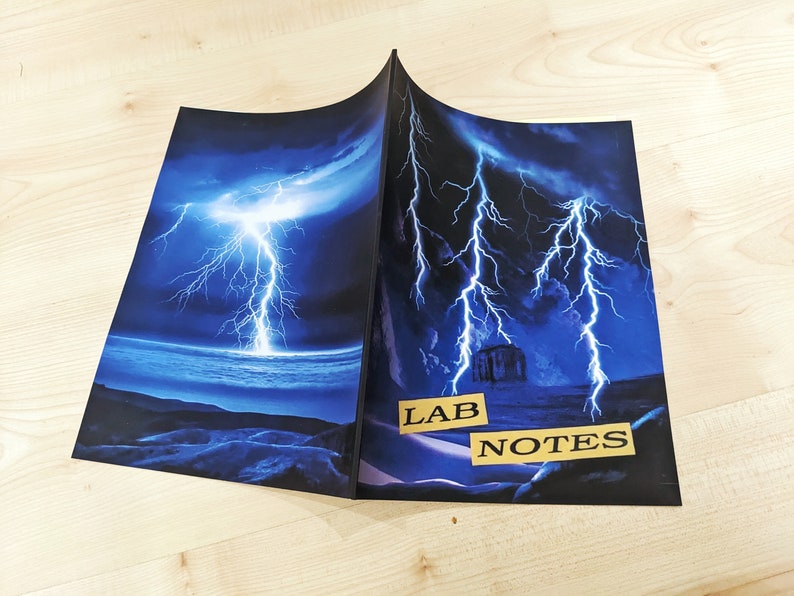 May include: A black notebook with a blue lightning bolt design on the cover. The cover has the words "LAB NOTES" printed on it in gold letters.