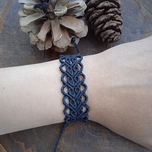 May include: A black macrame bracelet with a delicate, intricate pattern. The bracelet is tied with a knot at the end, allowing for adjustment.