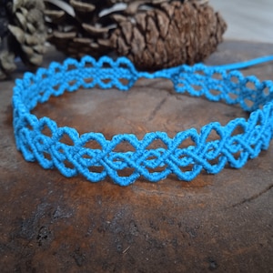 May include: A turquoise blue macrame choker necklace with a delicate, intricate pattern. The necklace is made with a single strand of cord and is tied in a knot at the back.