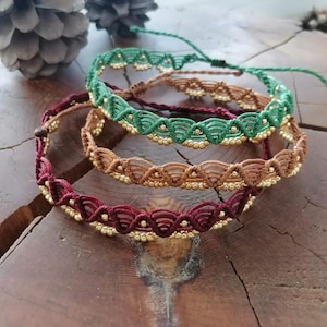 May include: Three layered bracelets with a woven design and gold beads. The bracelets are in shades of green, brown, and burgundy.