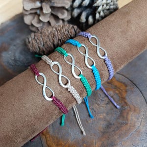 Puede incluir: Un conjunto de ocho pulseras con símbolo de infinito en varios colores, incluyendo morado, azul, verde y rojo. Las pulseras están hechas con un patrón de nudo simple y presentan un encanto de infinito plateado.