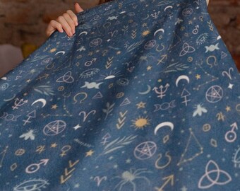 May include: A blue blanket with a celestial pattern featuring moons, stars, and astrological symbols. The blanket is held up by a person, partially obscuring their face. The background includes a brick wall and a wooden framed mirror.