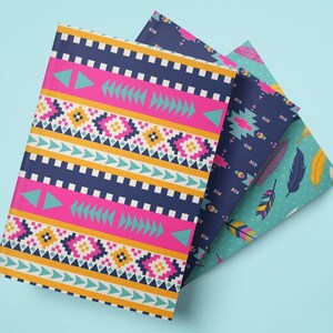 May include: Three notebooks with colorful patterned covers are fanned out on a light blue surface. The top notebook has a pink, navy, and yellow geometric design. The other two notebooks have navy and teal covers with feather and geometric patterns.