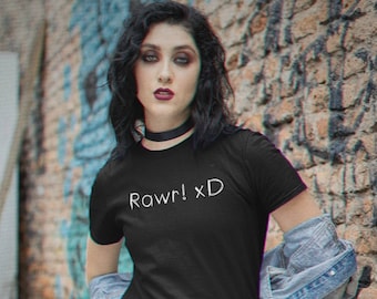 May include: Black t-shirt with the text "Rawr! xD" in white. The person is wearing a red and black plaid pleated skirt and a denim jacket. The background is a brick wall with graffiti.