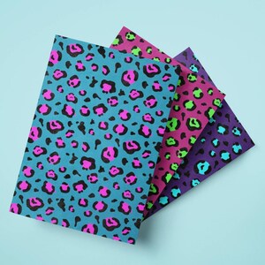 May include: Four sheets of paper with a leopard print design in various colors. The sheets are teal, pink, purple, and green, with black spots. The sheets are arranged in a fan shape against a light blue background.