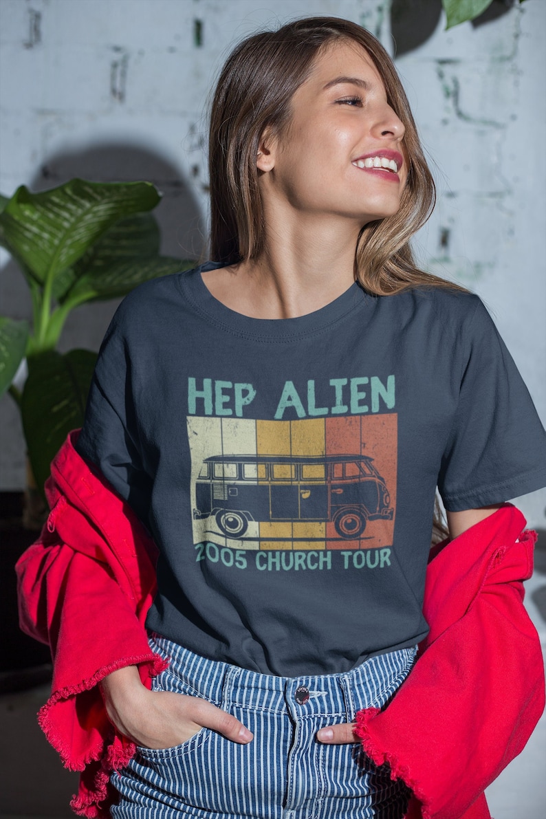 Peut inclure: T-shirt bleu marine avec l'inscription "HEP ALIEN 2005 CHURCH TOUR" et une illustration de van r&eacute;tro. La personne porte un jean ray&eacute; bleu et blanc et une veste rouge.
