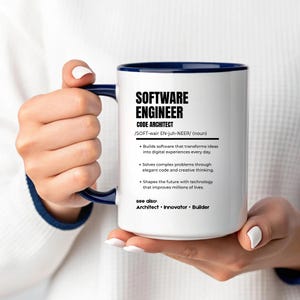 K&ouml;nnte beinhalten: Ein wei&szlig;er Keramikbecher mit dunkelblauem Innenraum und Henkel, der mit schwarzem Text bedruckt ist, welcher einen Softwareentwickler als Code-Architekten definiert, inklusive Aufz&auml;hlungspunkten &uuml;ber Softwareentwicklung und Probleml&ouml;sung.
