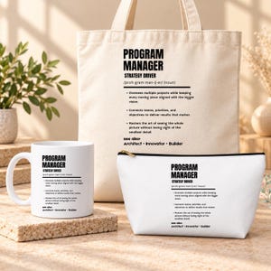 May include: A beige canvas tote bag, a white ceramic mug, and a white zippered pouch, each printed with black text defining a Program Manager as a strategy driver, including bullet points about project oversight and team connection.