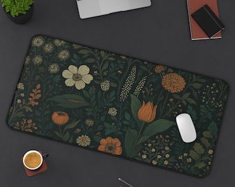 Puede incluir: Una alfombrilla de escritorio verde oscuro con un estampado floral con flores y follaje crema, naranja y dorado. Un ratón de ordenador blanco descansa sobre la alfombrilla, junto con un portátil, un cuaderno y lápices.