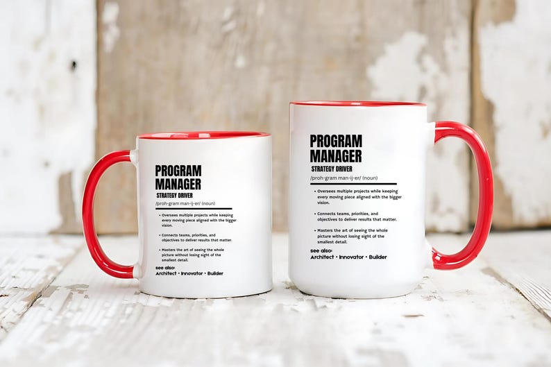 May include: Two white ceramic mugs with bright red interiors and handles. Each mug features black printed text defining a Program Manager as a strategy driver, including bulleted job responsibilities and a see also section listing Architect, Innovator, and Builder.