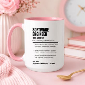 K&ouml;nnte beinhalten: Ein wei&szlig;er Keramikbecher mit einem zartrosa Innenraum und Henkel. Auf der Vorderseite befindet sich ein schwarzer Text, der einen Software-Ingenieur als Code-Architekten definiert, inklusive Aufz&auml;hlungspunkten zu Softwareentwicklung.