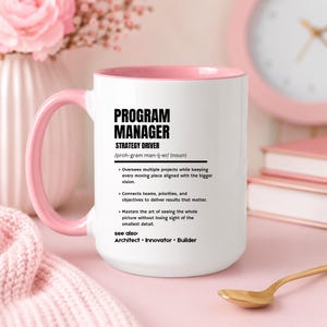 May include: A white ceramic mug with a pink interior and handle, featuring black text that defines a Program Manager as a strategy driver, including bulleted job responsibilities and the related terms Architect, Innovator, and Builder.