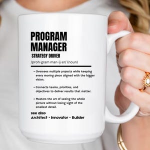 May include: A white ceramic mug featuring black printed text that defines a Program Manager as a strategy driver. The text includes a phonetic pronunciation, a bulleted list of professional responsibilities, and a see also section with the terms Architect, Innovator, and Builder.