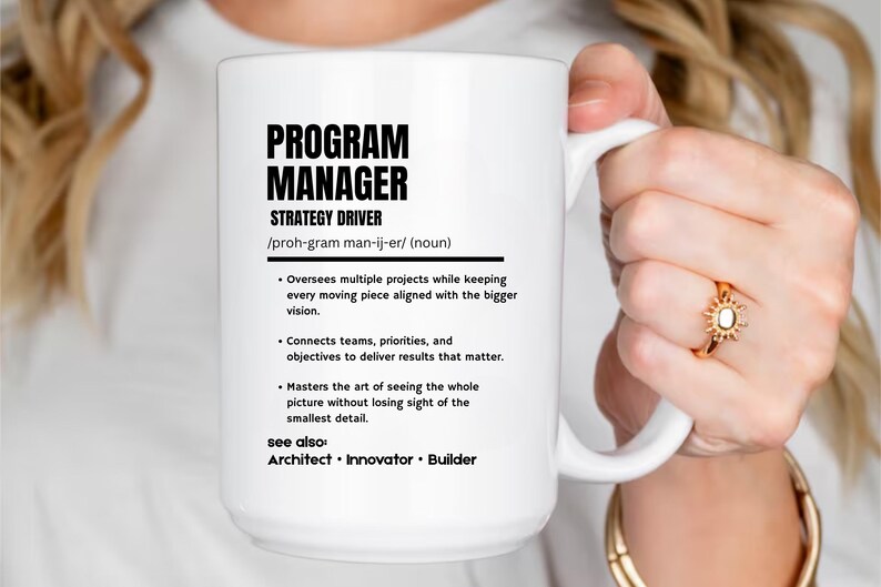 May include: A white ceramic mug featuring black printed text that defines a Program Manager as a strategy driver. The text includes a phonetic pronunciation, a bulleted list of professional responsibilities, and a see also section with the terms Architect, Innovator, and Builder.