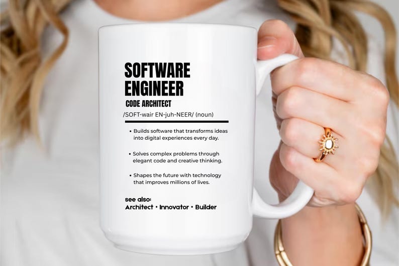 K&ouml;nnte beinhalten: Ein wei&szlig;er Keramikbecher mit schwarzem Text, der einen Softwareingenieur als Code-Architekten definiert. Der Text enth&auml;lt eine phonetische Aussprache, stichpunktartige Beschreibungen der beruflichen Aufgaben und einen Abschnitt siehe auch mit den Begriffen Architekt, Innovator und Erbauer.