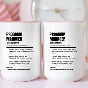 May include: Two white ceramic mugs with light pink handles and interiors. Each mug features black text defining a Program Manager as a strategy driver, including bullet points about overseeing projects, connecting teams, and mastering details.